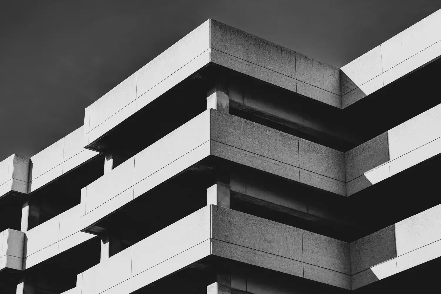 Stacked exposed concrete balconies on a brutalist building, shot in black and white against a dark sky