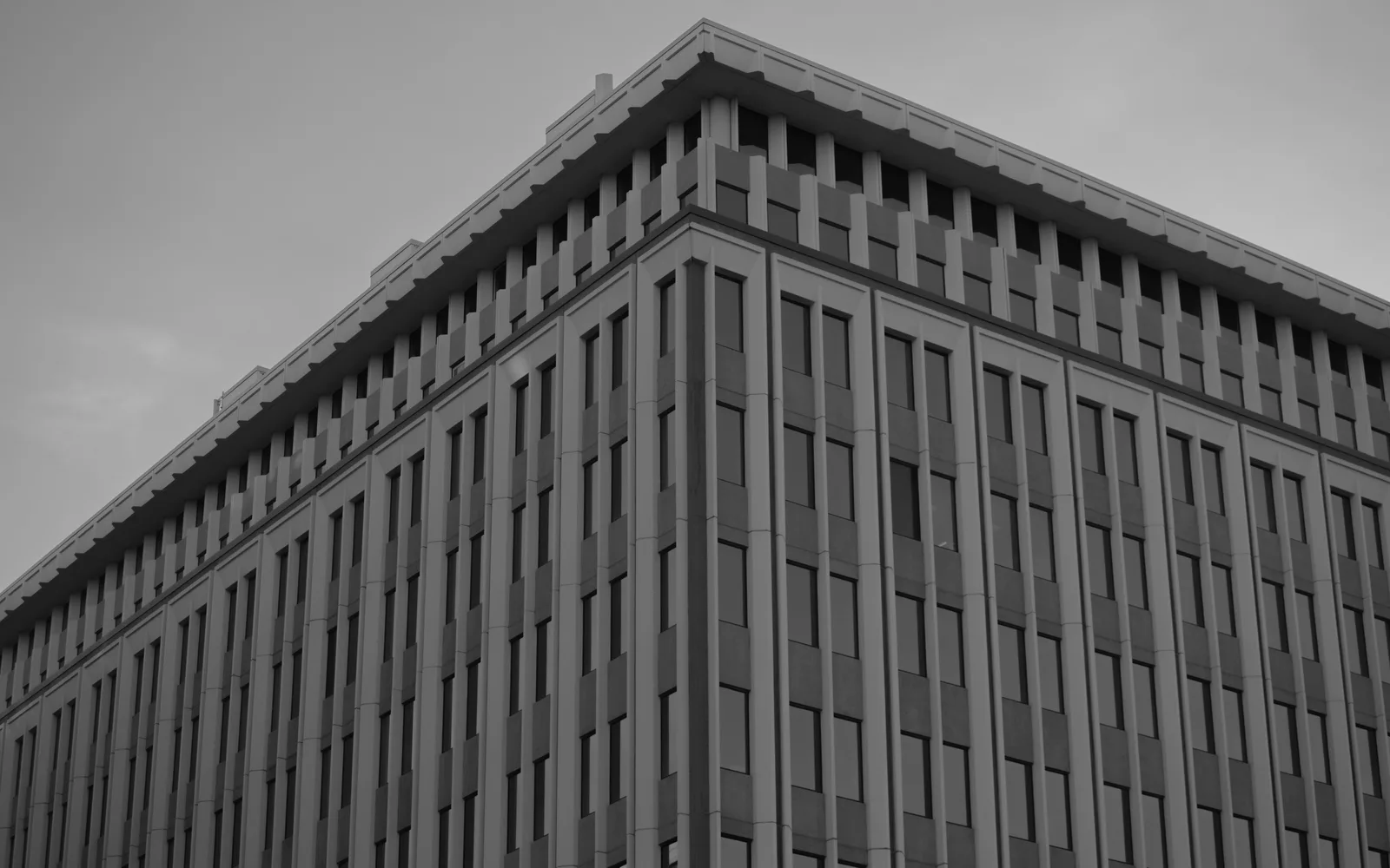 Corner of an office block whose repeated window bays visibly compress as each facade recedes